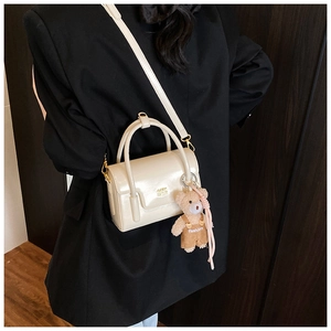 Detailansicht der cremefarbenen Lackleder-Handtasche mit Bärenanhänger und Goldlogo