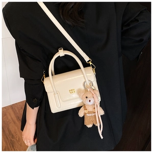 Detail der cremefarbenen Umhängetasche mit Goldlogo und Bärenanhänger am Model