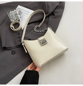 Close-up of beige leather crescent shoulder bag with silver chain and geometric buckle