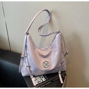 Détail du sac hobo violet clair avec logo M métallique sur des livres et un canapé
