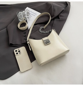 Detail of cream leather shoulder bag with silver chain and magnetic buckle on grey blazer