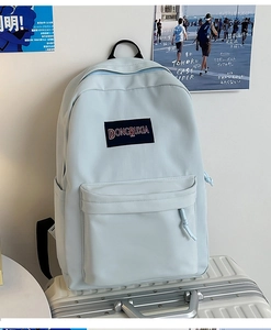 Detalle de mochila informal de nailon azul claro sobre una maleta blanca para viajes y clase