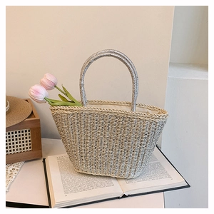 Close-up of handwoven beige straw tote with metallic silver threads and round metal handles