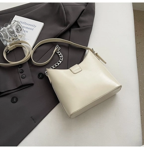 Close-up of beige glossy leather bag with silver chain strap and modern styling elements