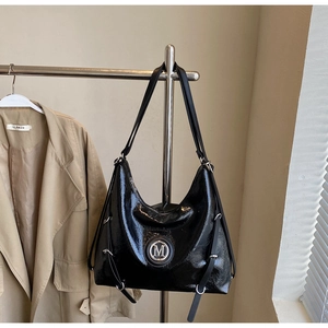 Détail d'un cabas en cuir noir brillant avec un logo M métallique rond élégant