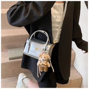 Chic silver metallic crossbody bag with a plush bear charm on a model in a black blazer