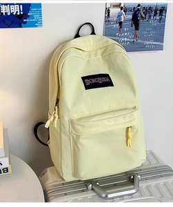 Detalle de mochila amarilla clara sobre maleta plateada con fondo minimalista de campus