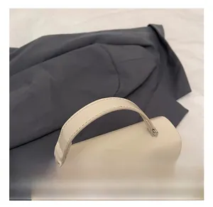 Dettaglio del manico della borsa in pelle crema con finiture in metallo argento e cuciture
