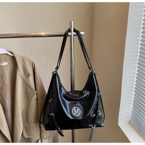 Détail d'un sac hobo noir brillant avec logo M métallique sur un cintre en inox