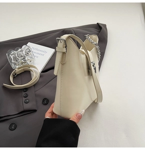 Close-up of cream shoulder bag featuring silver chain detail and leather strap over a blazer