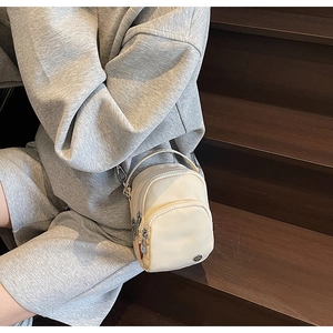 Détail d'un sac bandoulière en nylon blanc avec compartiments zippés sur l'escalier