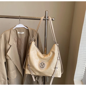 Détail du sac Hobo beige avec logo M en métal et cordons de serrage latéraux décoratifs
