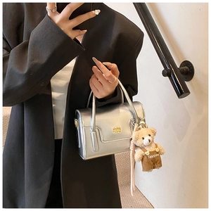 Detail der silbernen Metallic-Handtasche mit Bärenanhänger und goldenem Logo auf schwarzem Anzug