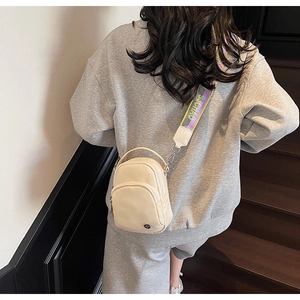 Détail d'un sac bandoulière en nylon beige avec large sangle à lettres sur modèle