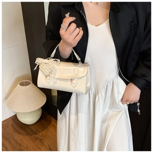 Dettaglio di una borsa bianco crema con fiocco in pizzo e ciondolo a cuore perlato