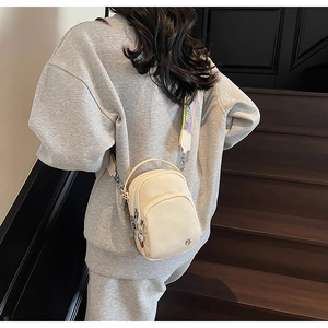 Sac bandoulière beige avec bandoulière tissée arc-en-ciel portée par un mannequin
