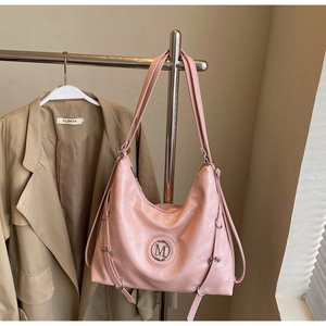 Détail du sac cabas en cuir rose avec logo M suspendu à côté d'un trench-coat élégant