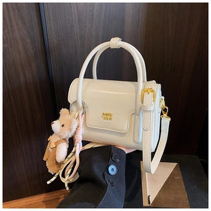 Detail der cremeweißen Lederhandtasche mit goldenem Logo und braunem Bär-Anhänger