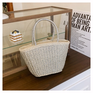 Detail of beige woven tote bag featuring shiny silver ring handles for a beach resort style