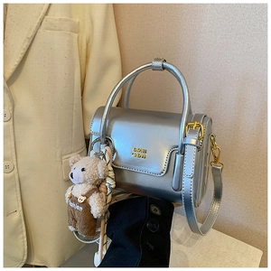 Detail der silbernen Spiegeltasche mit Gold-Logo und Plüschbär-Anänger für Damen