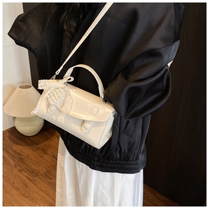 Dettaglio mini borsa squadrata bianco crema con ciondolo a fiocco di perle e pelle opaca