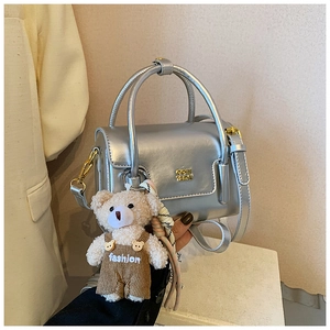 Nahaufnahme der silbernen Handtasche mit goldenem Logo und süßem Bärenanhänger