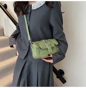 Close-up of matcha green crossbody bag with silver buckle worn by a model in a gray suit