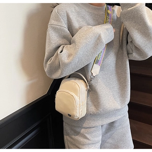 Gros plan d'un sac bandoulière en nylon blanc cassé avec une sangle large bicolore
