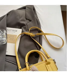 Detail of yellow lychee texture leather bucket bag with bow on grey blazer