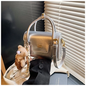 Macro detail of silver metallic square bag with gold logo and brown bear plush charm