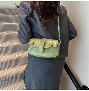 Detailed view of avocado green leather shoulder bag with metallic buckle on a grey suit