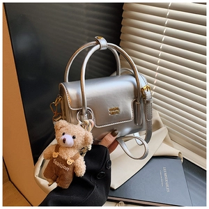 Detail einer silbernen Mini-Handtasche mit Metallic-Finish und Bärenanhänger