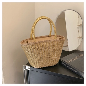 Dettaglio della borsa tote in paglia intrecciata dorata con eleganti manici e fodera interna