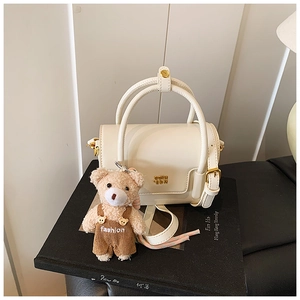 Detail of cream barrel handbag with gold hardware and a cute plush bear charm on a book