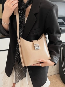 Minimalist beige hobo crossbody bag with silver buckle worn by a model in a black suit