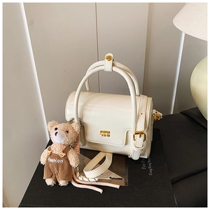 Detailed macro of cream faux leather handbag featuring a cute plush bear pendant and gold logo