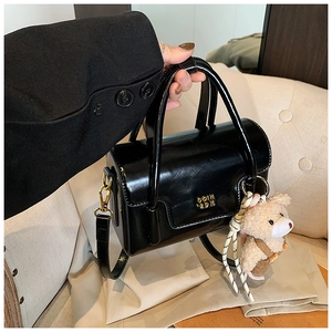 Close-up of black glossy small square bag with gold logo and plush bear charm