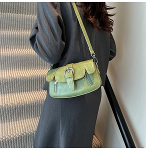 Green leather crossbody bag with silver buckle worn over a grey blazer on stairs