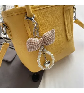Close-up of checkered bow keychain with pearls and heart pendant on yellow bucket bag