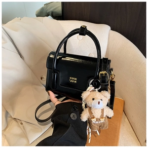 Close-up of black glossy leather square handbag with gold logo and cute bear charm detail