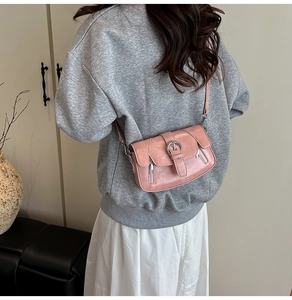 Pink crossbody bag with textured leather and metal buckle detail worn by a model