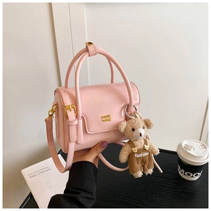 Detail of pink patent leather handbag with gold logo and cute bear charm accessory