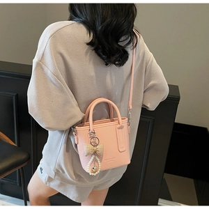 Detail of pink lychee leather bucket bag with pearl bow pendant worn on shoulder