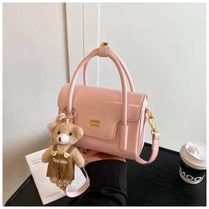 Detailed shot of pink glossy crossbody bag featuring a plush bear charm and golden logo