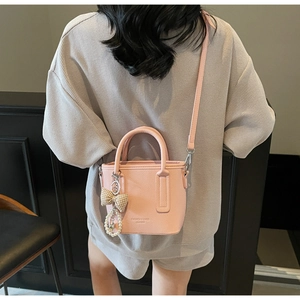 Detail of pink pebbled leather bucket bag featuring a plaid bow and pearl charm