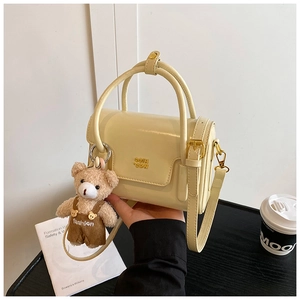 Detail view of cream-yellow PU leather handbag with gold metal logo and plush bear charm