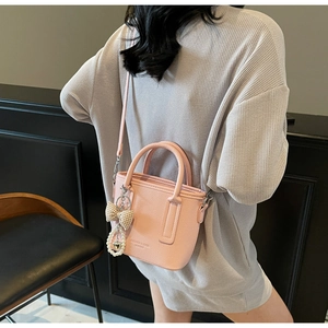 Pink lychee leather bucket bag with elegant pearl bow charm shown on model