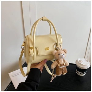 Detail of cream square handbag with gold logo, teddy bear pendant and shoulder strap