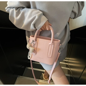 Pink lychee grain leather bucket bag with plaid bow and pearl charm shown on stairs