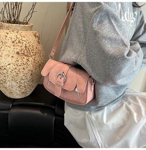 Close-up of pink shoulder bag with metal buckle and decorative zippers on matte faux leather